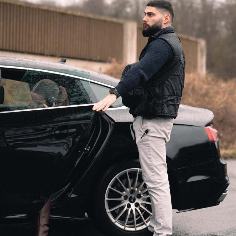 Personenchutz in Köln & deutschlandweit. Derlo CP Ein Mann steht an einem schwarzen Auto und öffnet die Tür.
